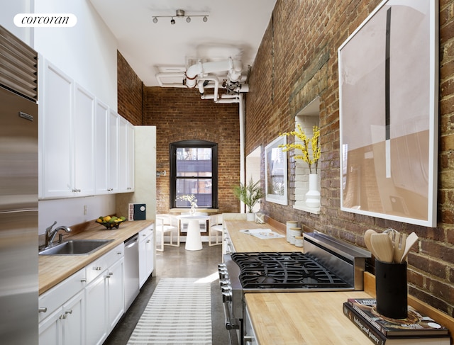 kitchen featuring a sink, wood counters, stainless steel appliances, and brick wall