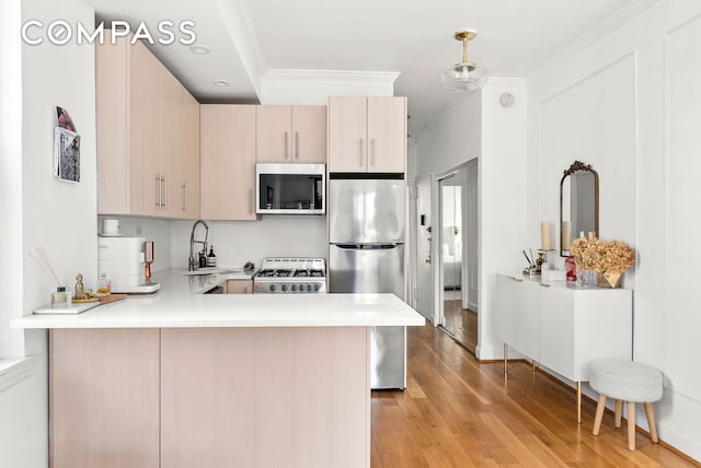 kitchen with appliances with stainless steel finishes, a peninsula, crown molding, light countertops, and light wood-style flooring