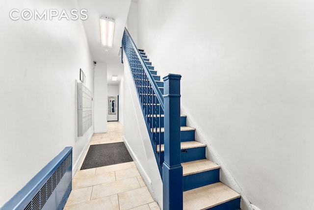 stairway with a towering ceiling, tile patterned flooring, and baseboards