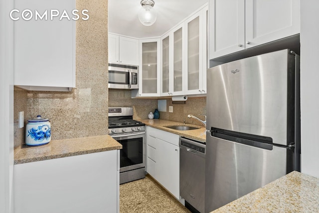 kitchen with a sink, appliances with stainless steel finishes, backsplash, and white cabinets