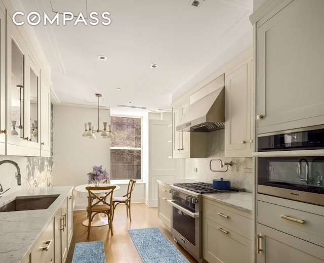 101 W 78th St Unit 3A, New York City, NY 10024 - kitchen featuring a sink, stainless steel appliances, wall chimney range hood, light stone counters, and light wood finished floors