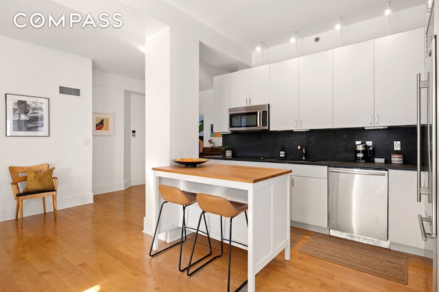 57 Front St Unit 303, New York City, NY 11201 - kitchen featuring appliances with stainless steel finishes, a kitchen bar, tasteful backsplash, light wood-style flooring, and white cabinetry