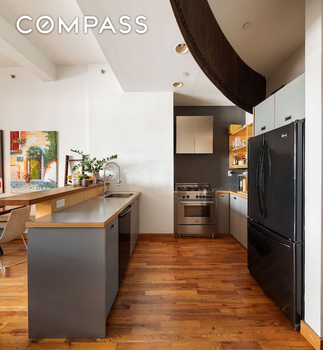 kitchen with freestanding refrigerator, a peninsula, light wood-style floors, a sink, and high end stainless steel range oven