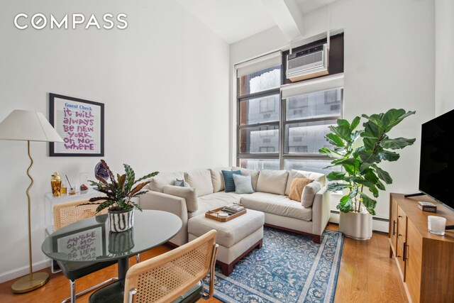 living room with light wood-style floors, beamed ceiling, baseboard heating, and a wall mounted AC