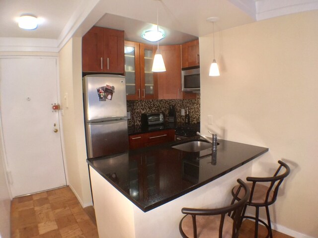 kitchen with appliances with stainless steel finishes, a sink, tasteful backsplash, a peninsula, and dark countertops