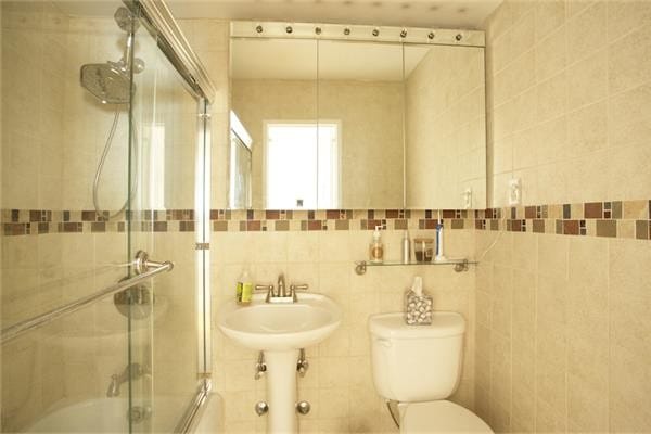full bath with tile walls, toilet, bath / shower combo with glass door, and a sink