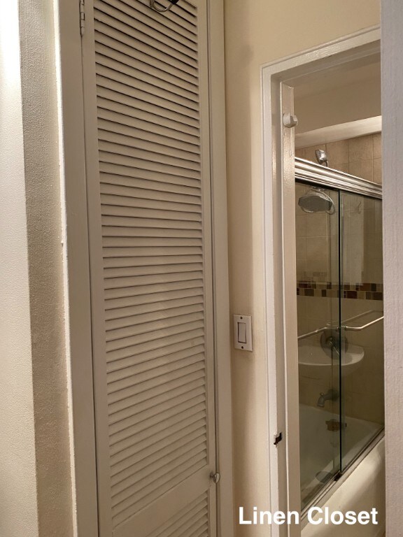 bathroom view of bath / shower combo with glass door and a closet