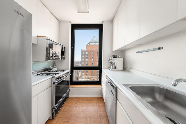 kitchen with a sink, modern cabinets, stainless steel appliances, light countertops, and white cabinetry