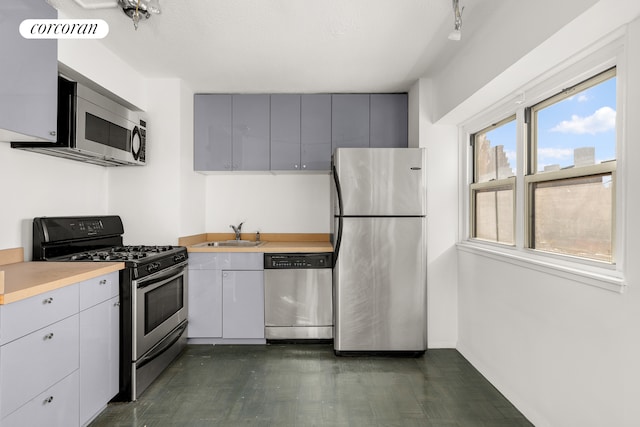 kitchen with appliances with stainless steel finishes, a sink, light countertops, baseboards, and gray cabinetry