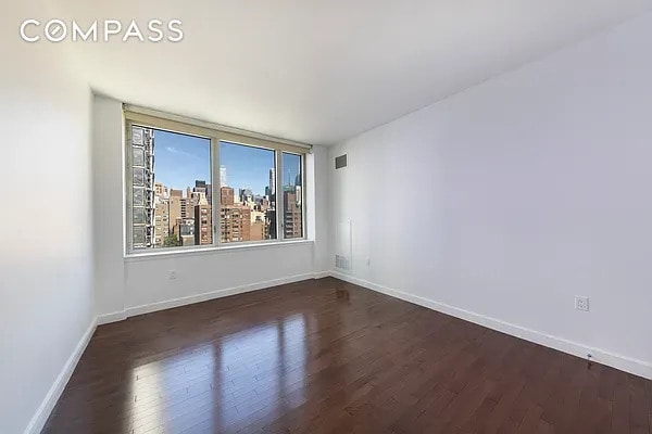 unfurnished room featuring baseboards, dark wood-style flooring, and a view of city