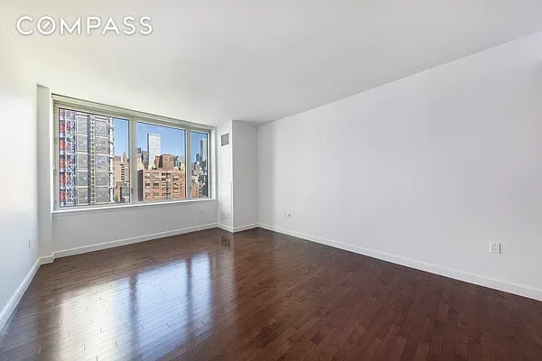 unfurnished room featuring baseboards, a city view, dark wood-style floors, and visible vents