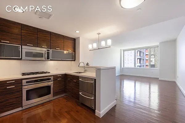 kitchen featuring baseboards, light countertops, a sink, dark wood finished floors, and stainless steel appliances