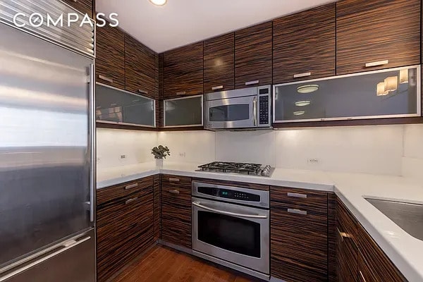 kitchen featuring modern cabinets, light countertops, dark wood-style floors, glass insert cabinets, and stainless steel appliances