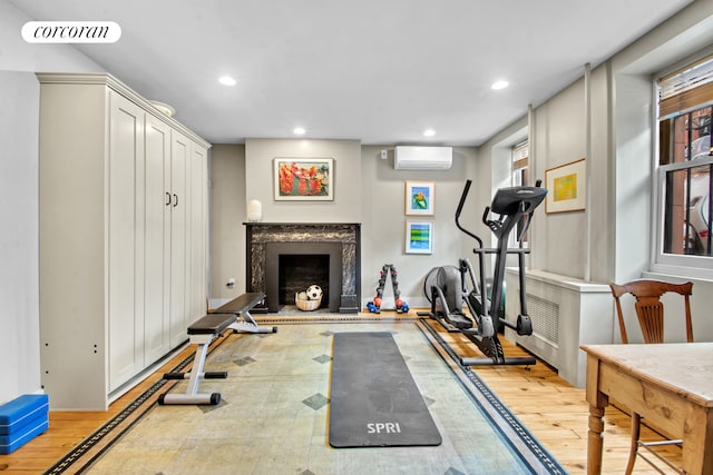 exercise room featuring light wood-style floors, a premium fireplace, recessed lighting, a wall unit AC, and visible vents