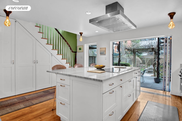 kitchen with a kitchen island, range hood, light wood-type flooring, light stone counters, and white cabinetry