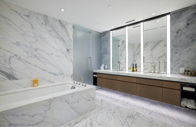 full bath with a tub with marble appearance, double vanity, marble tiled floors, and stone wall