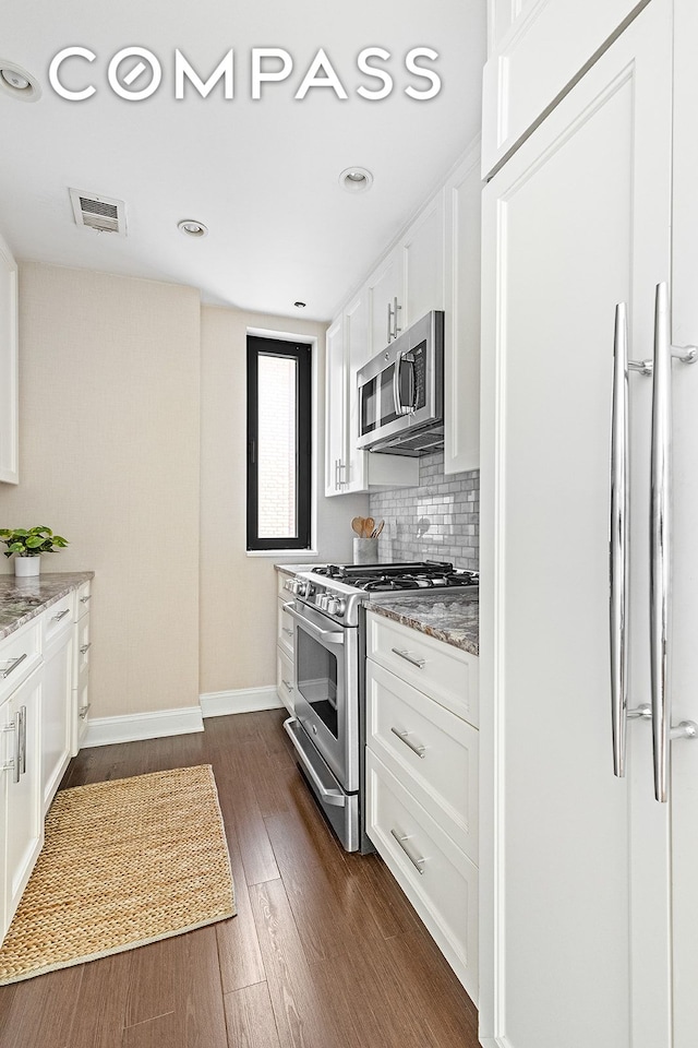 kitchen with appliances with stainless steel finishes, light stone counters, white cabinets, baseboards, and dark wood-type flooring