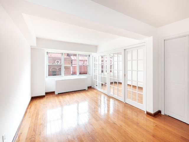 empty room featuring radiator heating unit, baseboards, french doors, and light wood-type flooring