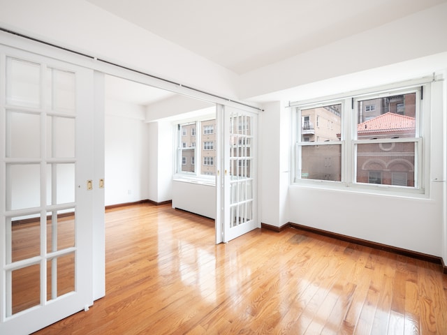 spare room featuring baseboards, french doors, and light wood-type flooring