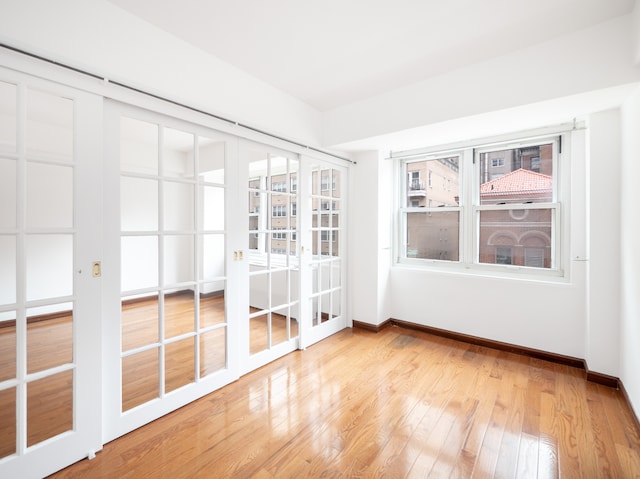 spare room featuring french doors, baseboards, and light wood-type flooring