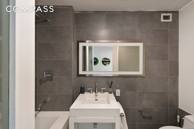 full bathroom featuring tile walls, toilet, vanity, washtub / shower combination, and backsplash