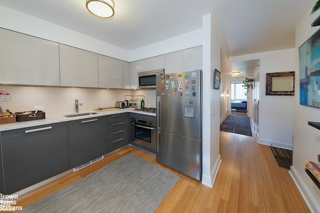 kitchen featuring appliances with stainless steel finishes, a sink, light countertops, modern cabinets, and light wood-type flooring