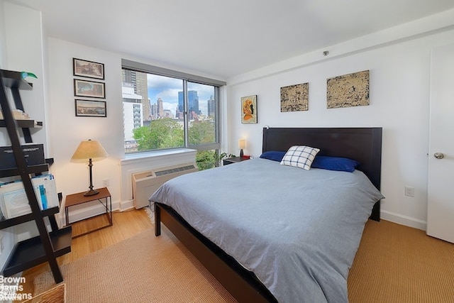 bedroom with wood finished floors, a wall mounted air conditioner, baseboards, and a view of city