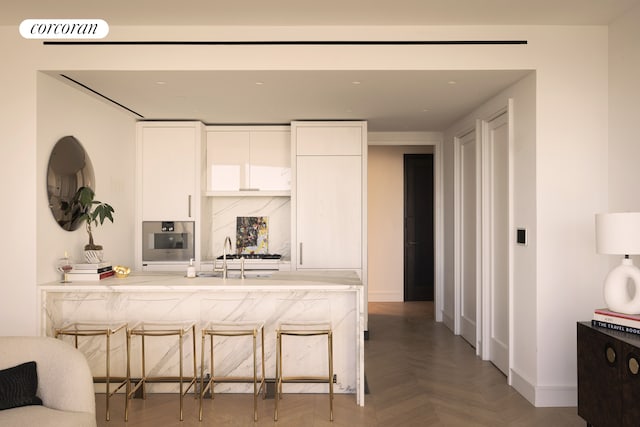 kitchen with a peninsula, oven, baseboards, and white cabinetry