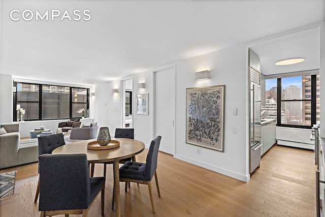 dining area with a baseboard heating unit, light wood-style floors, and baseboards