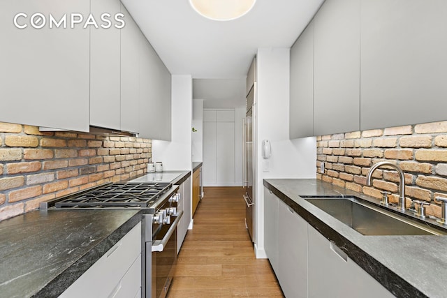 kitchen with light wood-style flooring, decorative backsplash, premium appliances, and a sink