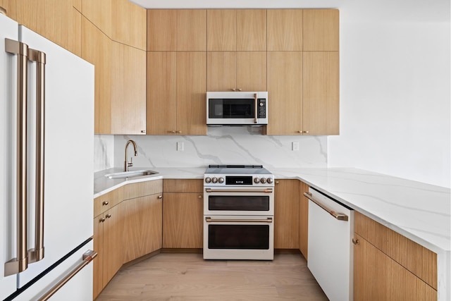 kitchen with high quality appliances, a sink, light stone counters, light wood-style floors, and a peninsula