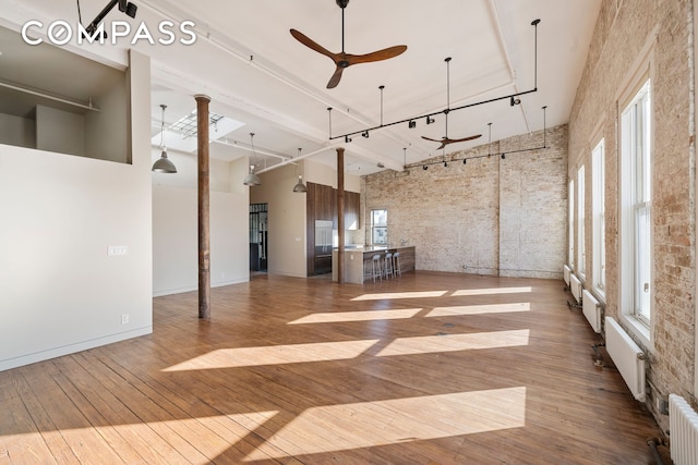 705 Driggs Ave Unit 13, New York City, NY 11211 - unfurnished living room featuring a towering ceiling, wood-type flooring, ceiling fan, radiator heating unit, and brick wall