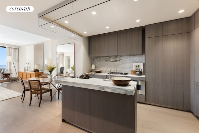 500 W 18th St Unit West9F, New York City, NY 10011 - kitchen with decorative backsplash, light wood finished floors, stainless steel appliances, modern cabinets, and a center island with sink