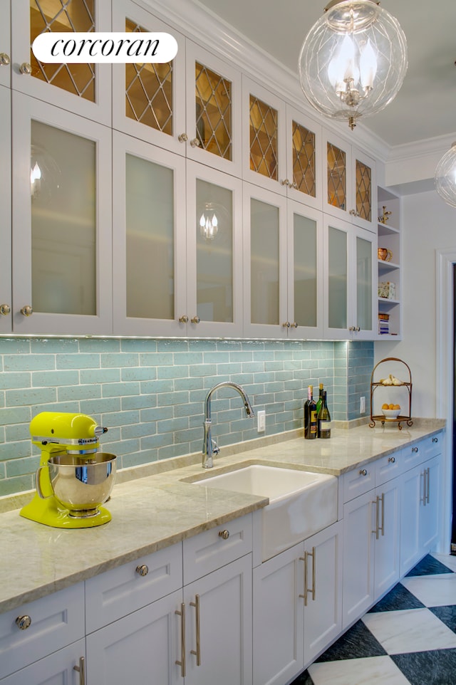 kitchen featuring white cabinetry, light stone counters, ornamental molding, and a sink