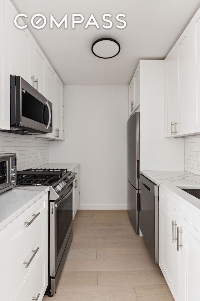 kitchen with appliances with stainless steel finishes, white cabinetry, light stone countertops, light wood-style flooring, and decorative backsplash