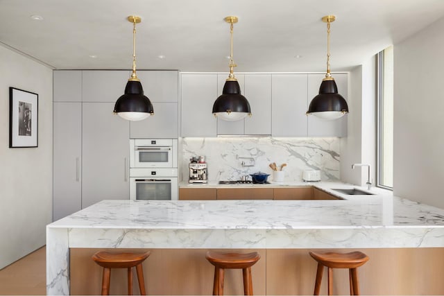 kitchen featuring a sink, modern cabinets, white double oven, a breakfast bar, and light stone countertops