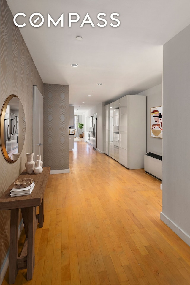corridor featuring baseboards, an accent wall, light wood finished floors, and wallpapered walls