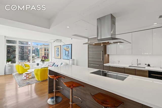 kitchen featuring modern cabinets, island range hood, light countertops, black electric cooktop, and a sink