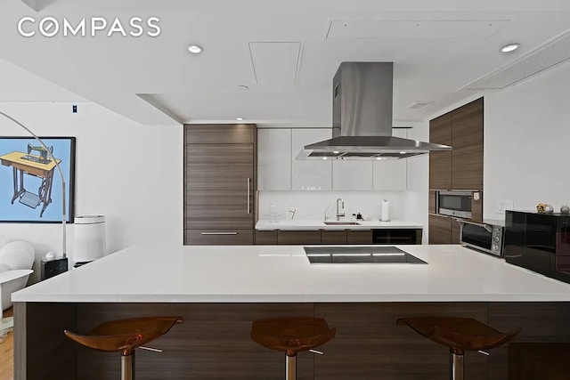 kitchen with electric stovetop, modern cabinets, island range hood, and a kitchen breakfast bar
