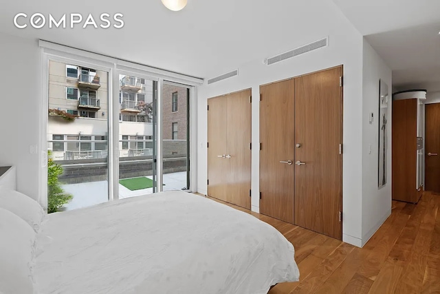 bedroom featuring access to exterior, light wood finished floors, two closets, and visible vents