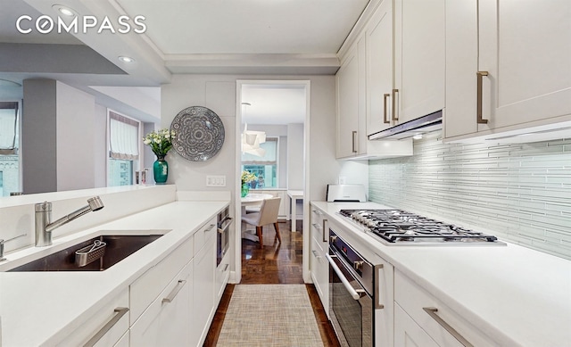 kitchen with a sink, stainless steel appliances, white cabinetry, light countertops, and under cabinet range hood