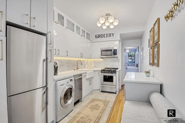 kitchen with white cabinetry, washer / clothes dryer, a sink, stainless steel appliances, and backsplash