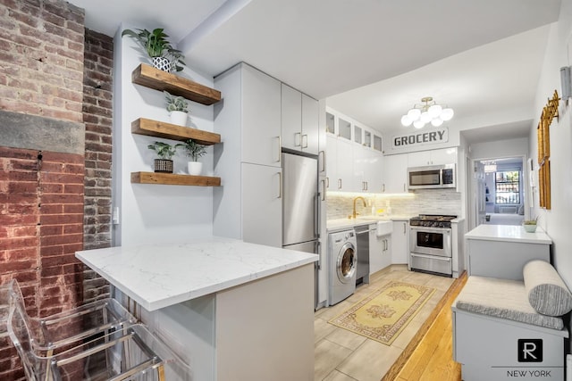 kitchen featuring open shelves, washer / dryer, tasteful backsplash, light stone counters, and appliances with stainless steel finishes