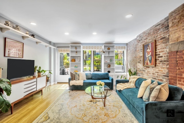 living area with baseboards, brick wall, wood finished floors, and plenty of natural light