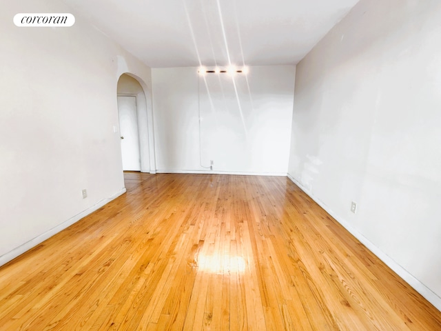 unfurnished room with visible vents, arched walkways, light wood-style flooring, and baseboards