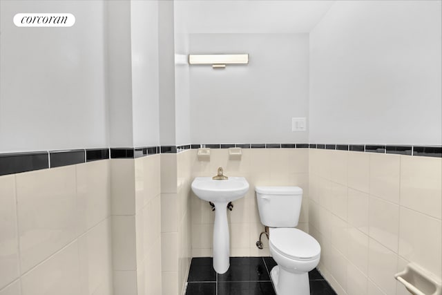 half bath featuring tile walls, toilet, wainscoting, and tile patterned flooring