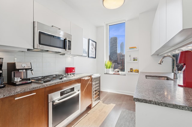 kitchen featuring appliances with stainless steel finishes, a sink, modern cabinets, backsplash, and light wood-style floors