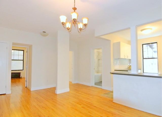 unfurnished dining area with light wood finished floors, baseboards, and an inviting chandelier