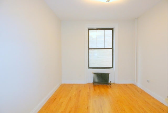 spare room featuring light wood-style flooring, radiator heating unit, and baseboards