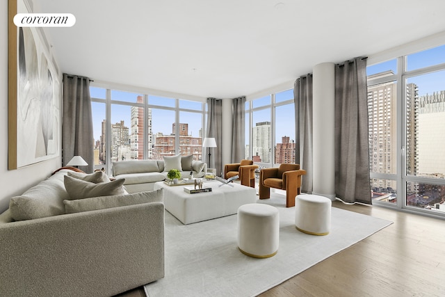 living area with a view of city, floor to ceiling windows, a healthy amount of sunlight, and wood finished floors